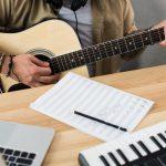 cropped shot of musician playing guitar at workplace with MPC pad and laptop