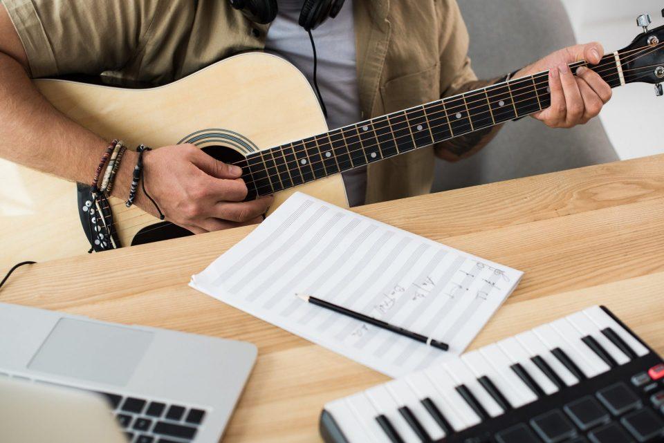 cropped shot of musician playing guitar at workplace with MPC pad and laptop